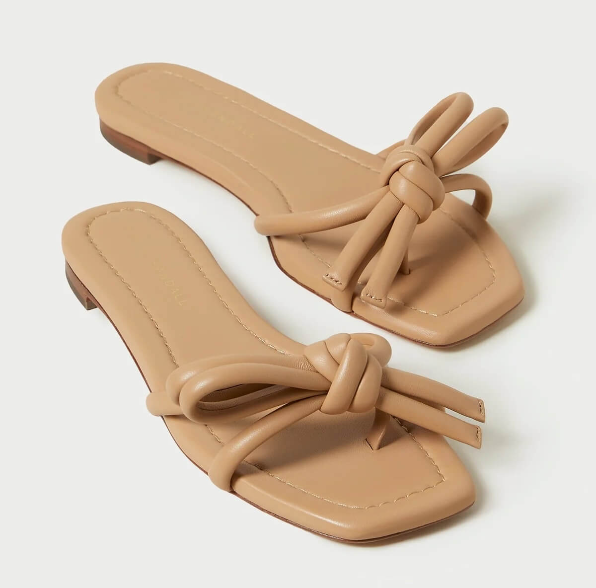 A pair of tan leather flat sandals with a knotted design on top, displayed on a white background.