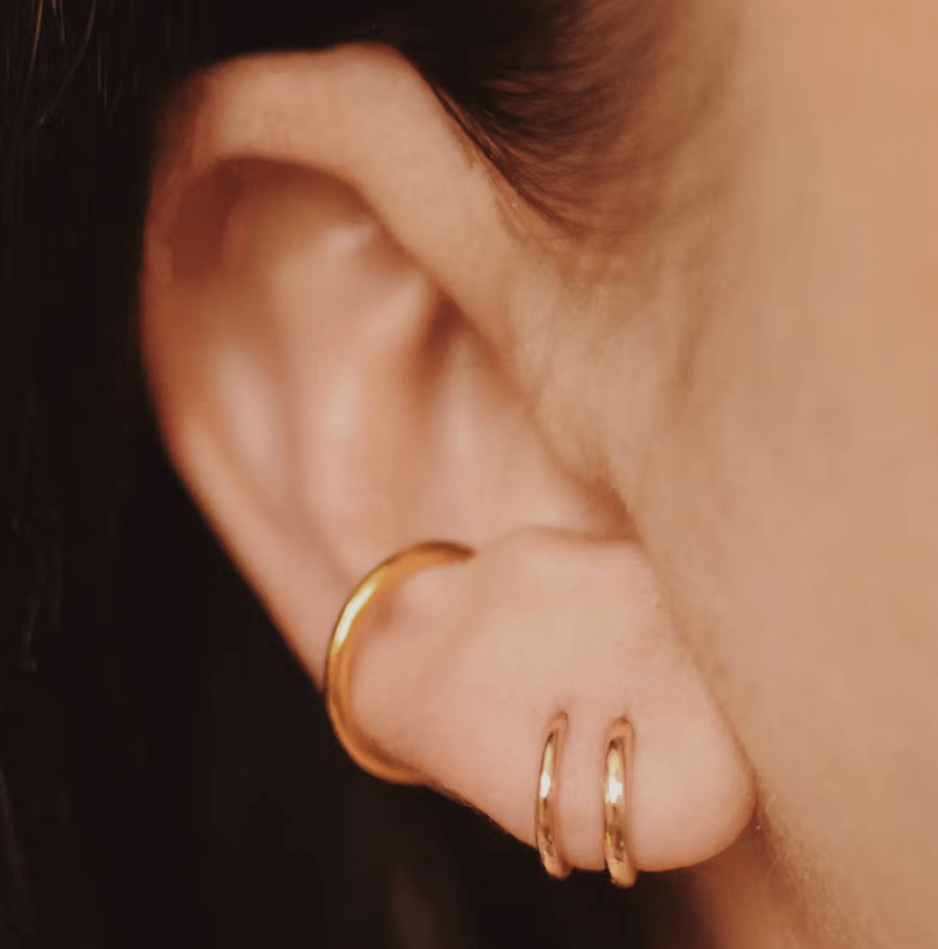 Close-up of a woman's ear adorned with gold hoop earrings.