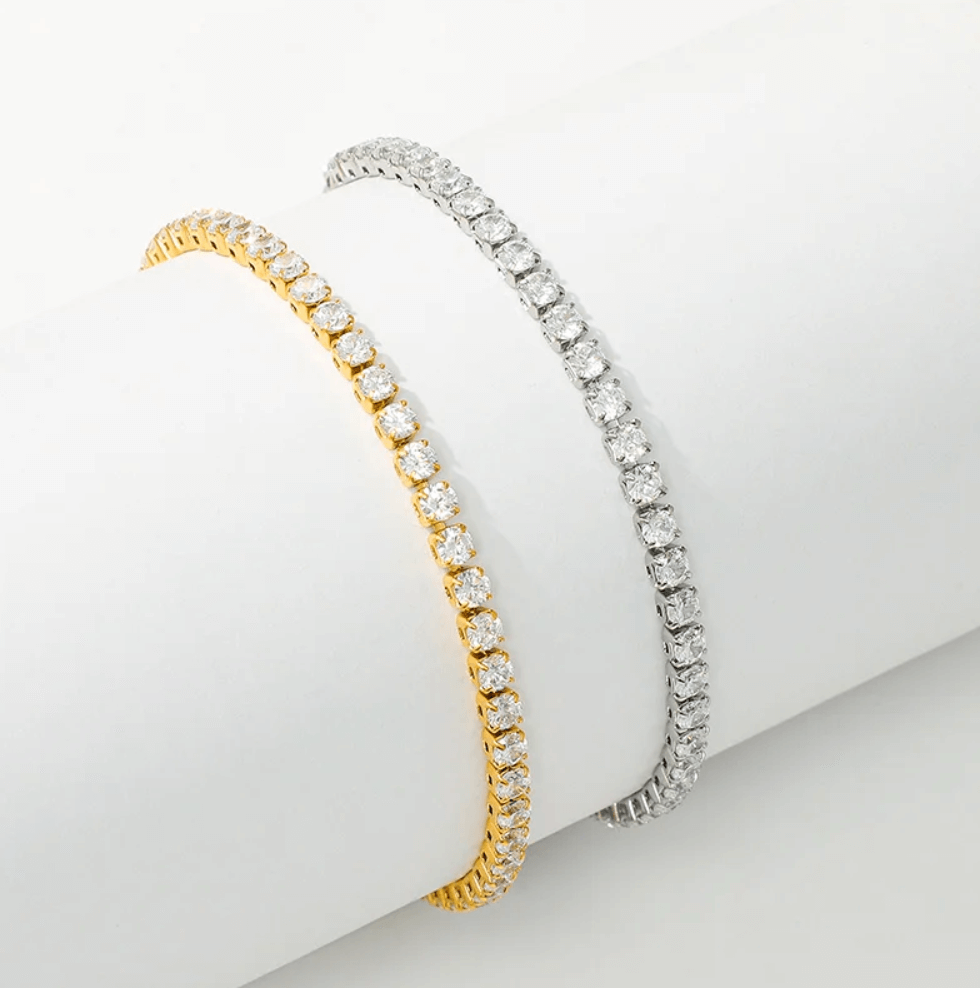 Two diamond tennis bracelets, one gold and one silver, displayed on a white cylindrical stand.