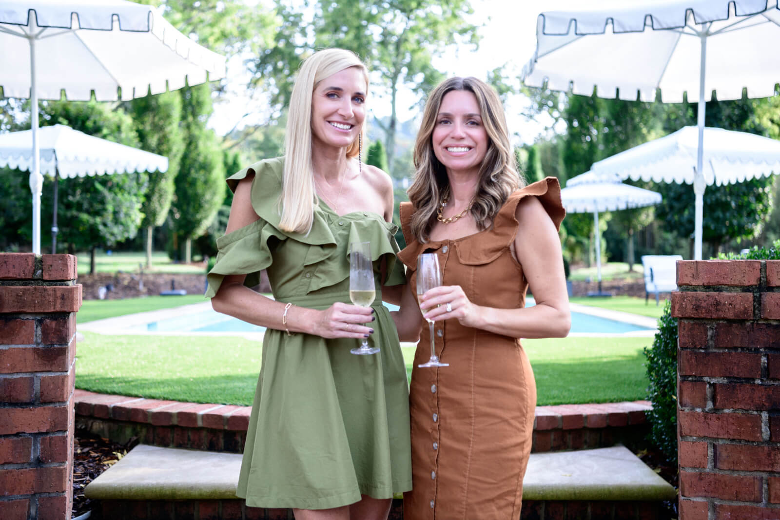 Two women smiling and holding champagne flutes at an outdoor event.