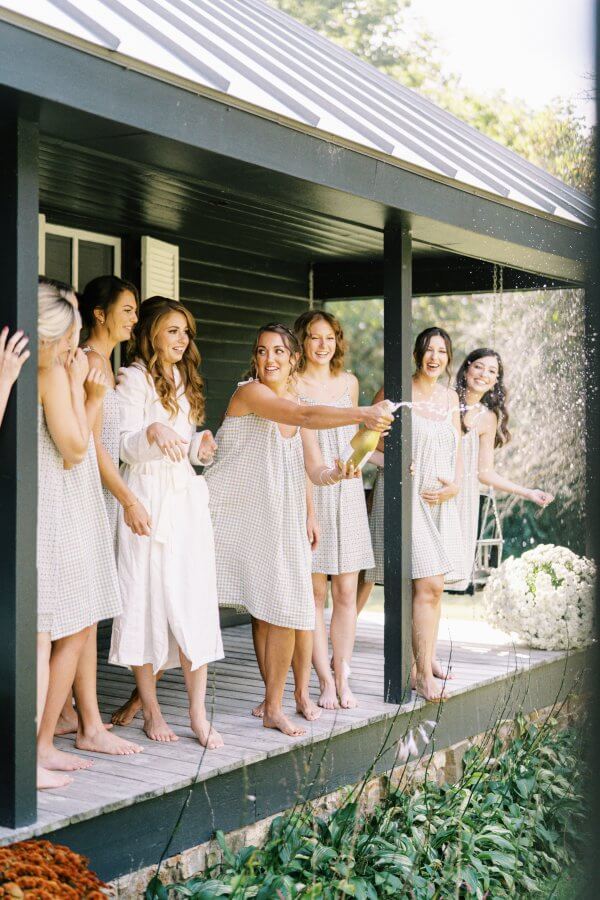 Group of women in matching dresses celebrating with champagne on a porch.
