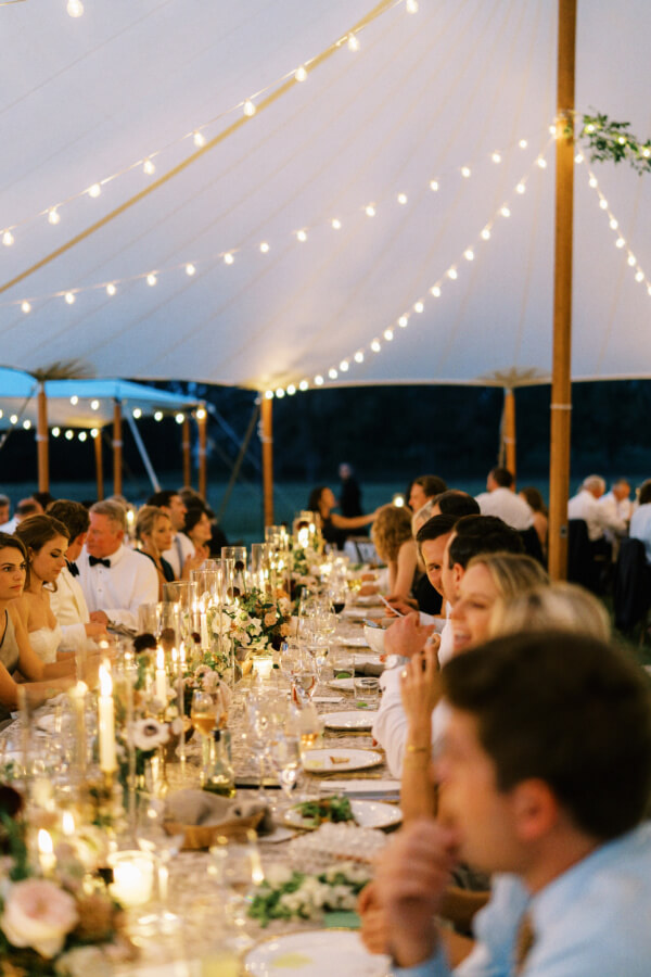 Elegant outdoor wedding reception with guests dining under string lights and a tent.
