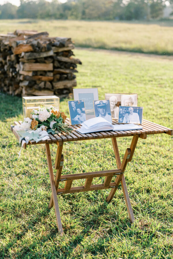 A wooden table set up in a grassy field displaying photographs, flowers, and a clear box, possibly as part of an event or gathering.