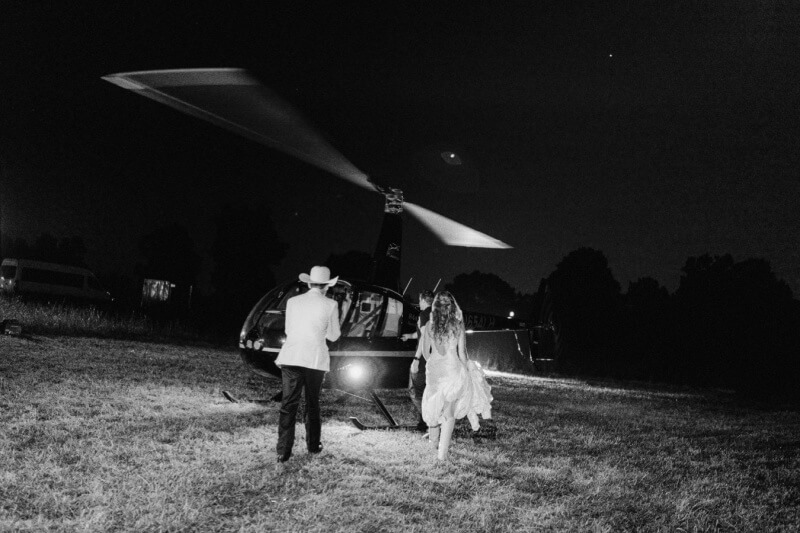 A bride and groom approach a helicopter at night for a dramatic departure.