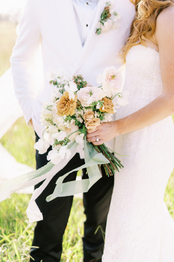 Bride and groom holding a bouquet of flowers together on their wedding day.
