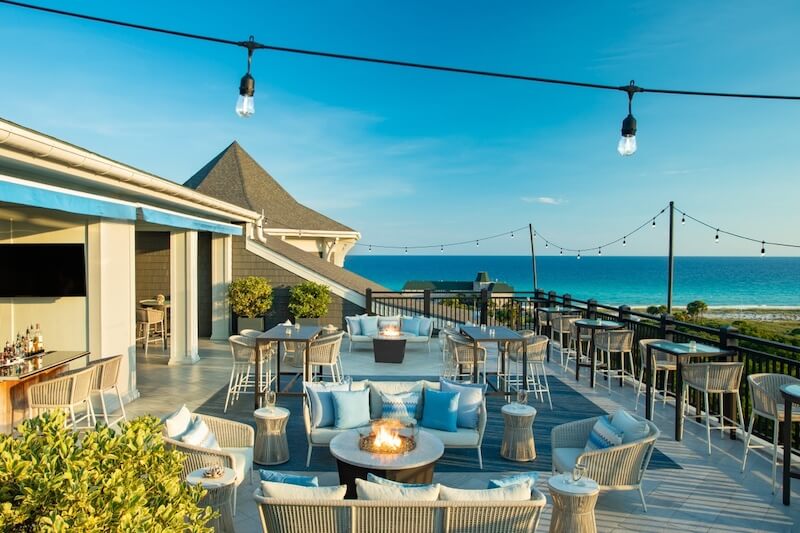9 Boutique Hotels on the Emerald Coast - 17 Oceanfront terrace with fire pit, string lights, and seating area overlooking the beach at one of the 30a hotels during daytime.