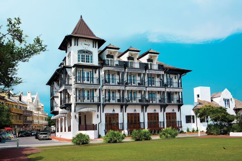 9 Boutique Hotels on the Emerald Coast - 11 Luxurious multi-story white building with black balconies, turret, and coastal 30a architectural style, situated near a green lawn under a blue sky.