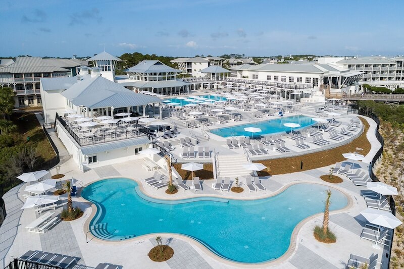 9 Boutique Hotels on the Emerald Coast - 13 Aerial view of a 30a resort with multiple swimming pools, loungers, and a central building with a white roof, surrounded by smaller white buildings.