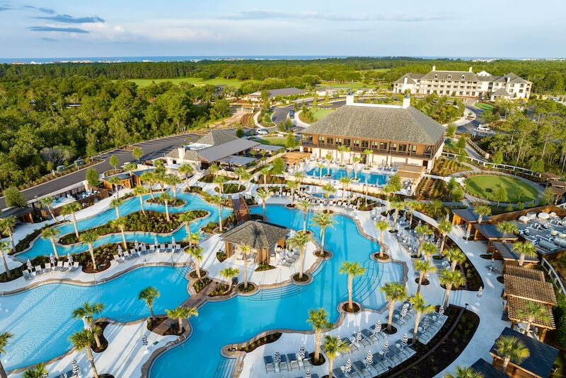 9 Boutique Hotels on the Emerald Coast - 1 Aerial view of a 30a hotel luxury resort with expansive swimming pools and sun loungers surrounded by lush greenery.