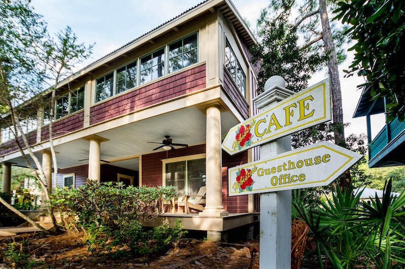 9 Boutique Hotels on the Emerald Coast - 3 Café and guesthouse office sign outside a two-story 30a hotels building with a porch and surrounded by trees.