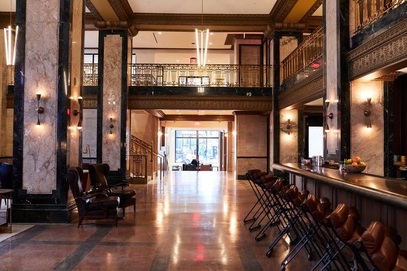 Spacious hotel lobby with marble floors, ornate railings, and a row of bar stools. Soft lighting and seating areas visible on the left. Large windows at the far end offer a glimpse into what makes it one of the best hotels in Nashville.