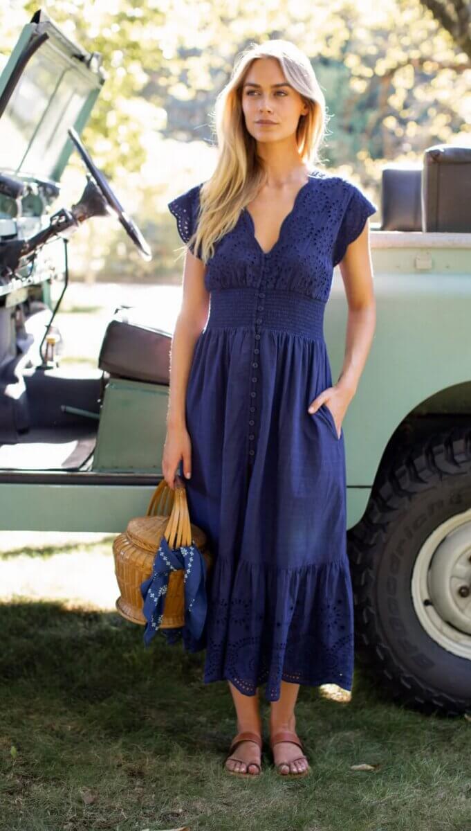 18 Birmingham FINDS for May Celebrations: Graduation, Mother's Day & More - 5 Woman in a navy blue dress stands beside a vintage green vehicle, holding a wicker handbag with a blue scarf; she is outdoors on grass showcasing Birmingham FINDS May style.