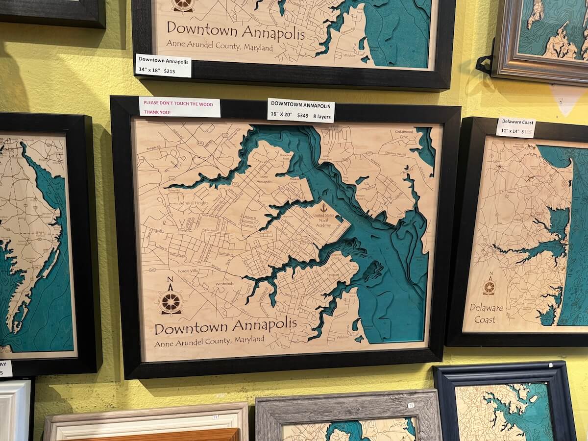 Wall display of various framed topographic laser-cut wooden maps of different regions, including annapolis and delaware coast.