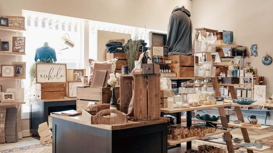A quaint shop interior featuring wooden shelves and tables displaying various home decor items, gifts, and clothing under soft lighting.