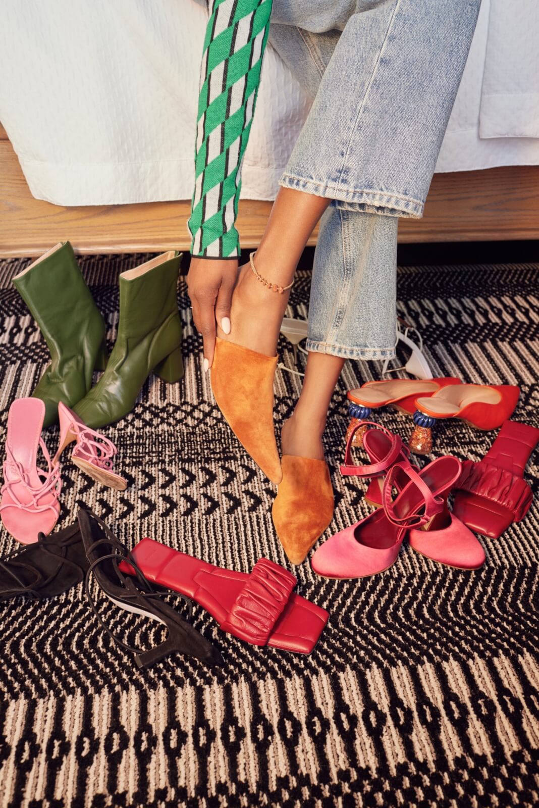 5 Local Experiences Every Memphian Should Try - 6 Person wearing jeans and a green sweater tries on orange suede mules, surrounded by various pairs of colorful shoes on a patterned rug.