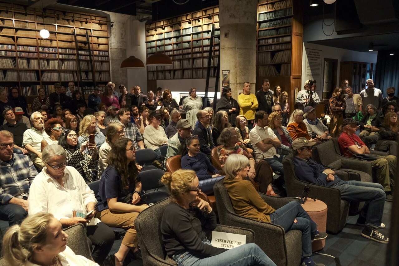 5 Local Experiences Every Memphian Should Try - 8 A large group of people seated and standing in a library or bookstore, attentively listening to a speaker or presentation. Vinyl records fill the background wall.