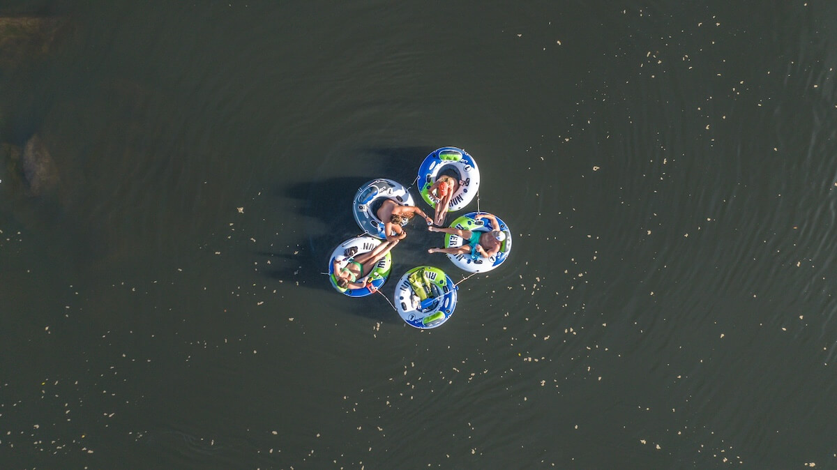 Aerial view of five people in individual colorful floating tubes on a river, forming a connected circle.