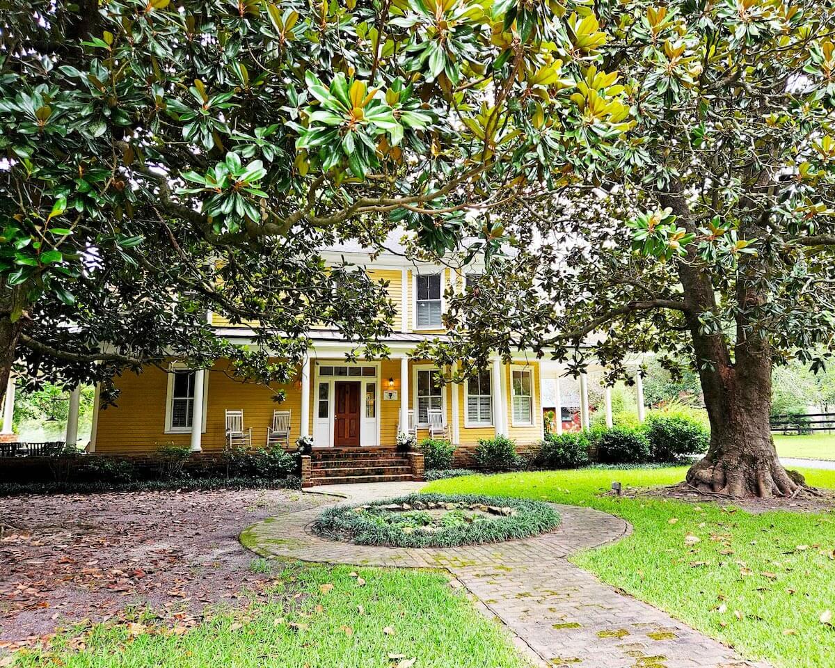 Exterior of yellow bed and breakfast with a tree in the front yard.