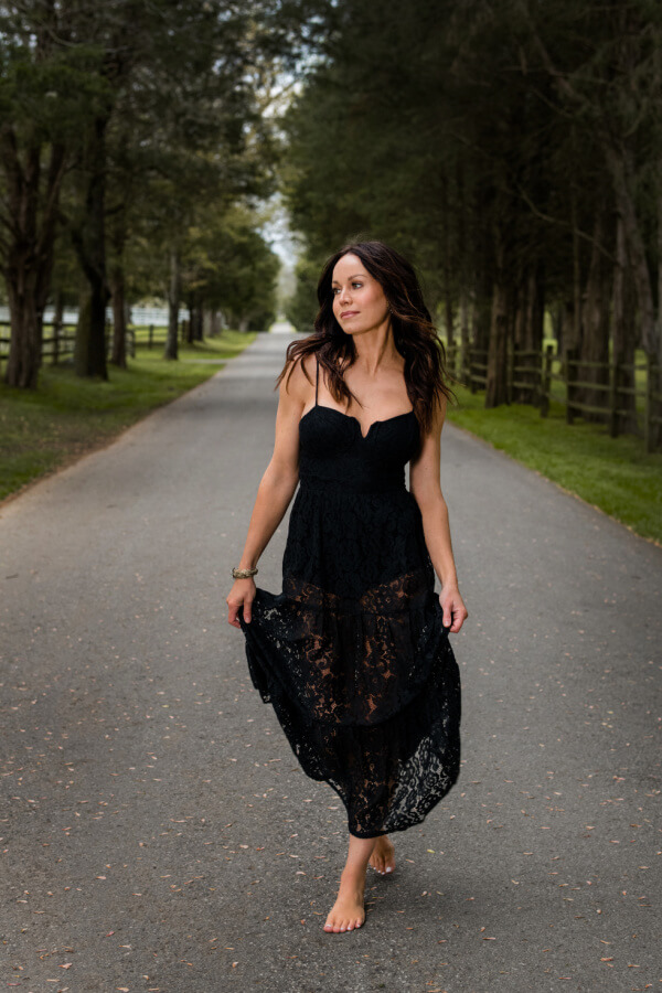 Woman in a black dress, walking along a treelined street