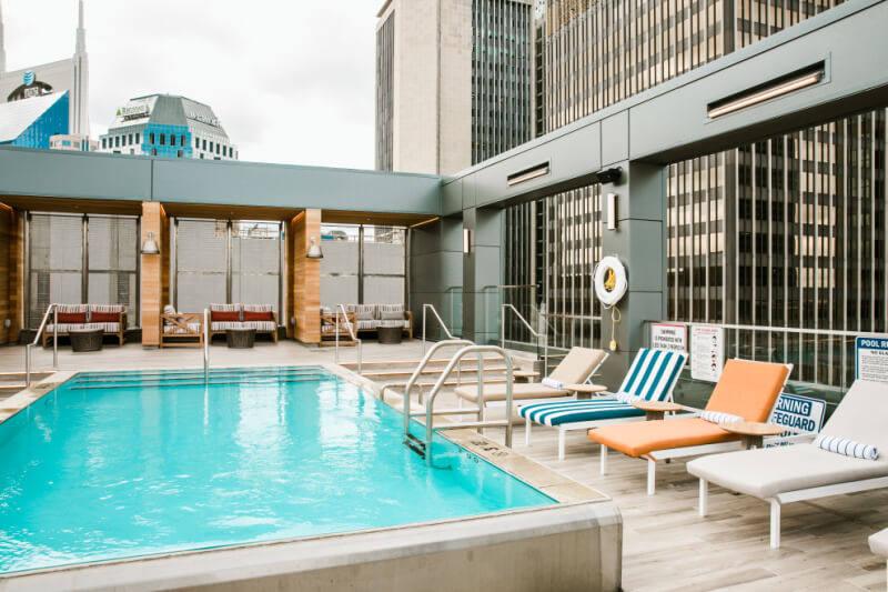 Rooftop swimming pool with lounge chairs and city skyscrapers in the background.