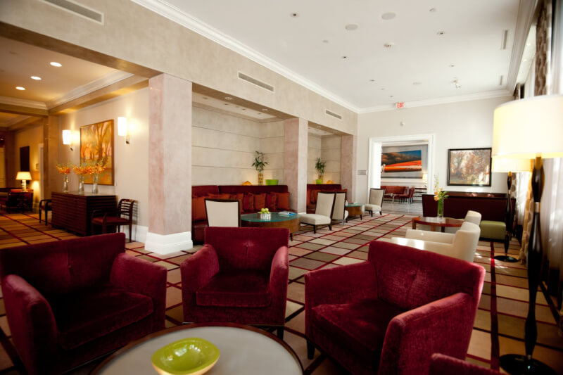 A modern hotel lobby in Mississippi featuring maroon armchairs, a checkered floor, wall art, and ambient lighting. This boutique hotel's seating area includes sofas and a coffee table with a green bowl.