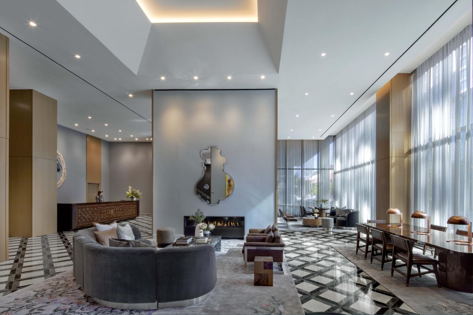 This modern lobby, found in one of the best hotels in Nashville, features stylish gray seating and a geometric-patterned floor. Large windows illuminate a central fireplace, while an abstract wall mirror and visible reception desk add decorative flair to this chic space.