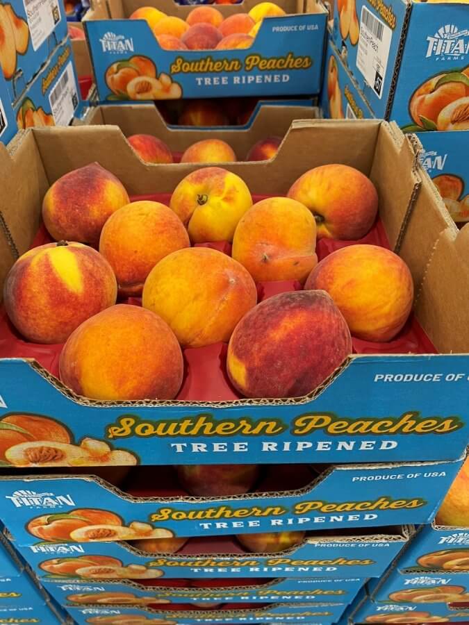 Boxes of ripe southern peaches from Titan Farms on display at a store, labeled "tree ripened" and "produce of USA.