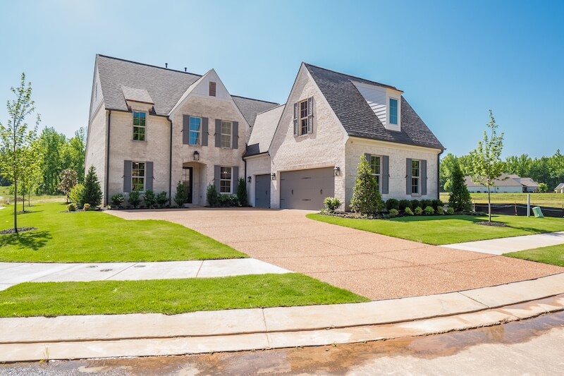 A large, two-story house with light-colored brick exterior, a double garage, and a spacious driveway is set on a neatly landscaped yard with young trees on Magnolia Ridge Drive in Rossville, Tennessee. The clear blue sky overhead completes this picturesque setting.