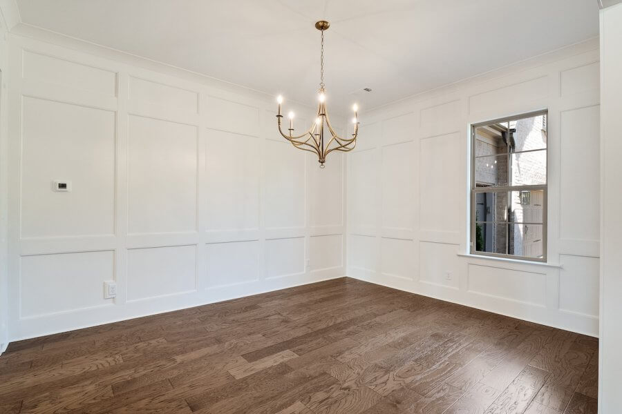 A minimalist empty room with white paneled walls, a wooden floor, a single window, and a gold chandelier hanging from the ceiling, similar to the elegant interiors found at 140 Magnolia Ridge Drive in Rossville, Tennessee.