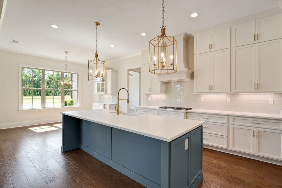 Modern kitchen with a large island featuring a blue base and white countertop, pendant lights, white cabinetry, stainless steel appliances, and hardwood floors. A window lets in natural light in this beautiful home at 140 Magnolia Ridge Drive, Rossville Tennessee.