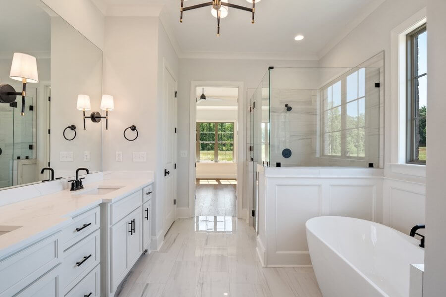 A modern bathroom on Magnolia Ridge Drive in Rossville, Tennessee, features a white double-sink vanity, a glass-enclosed shower, and a freestanding bathtub with large windows providing natural light.