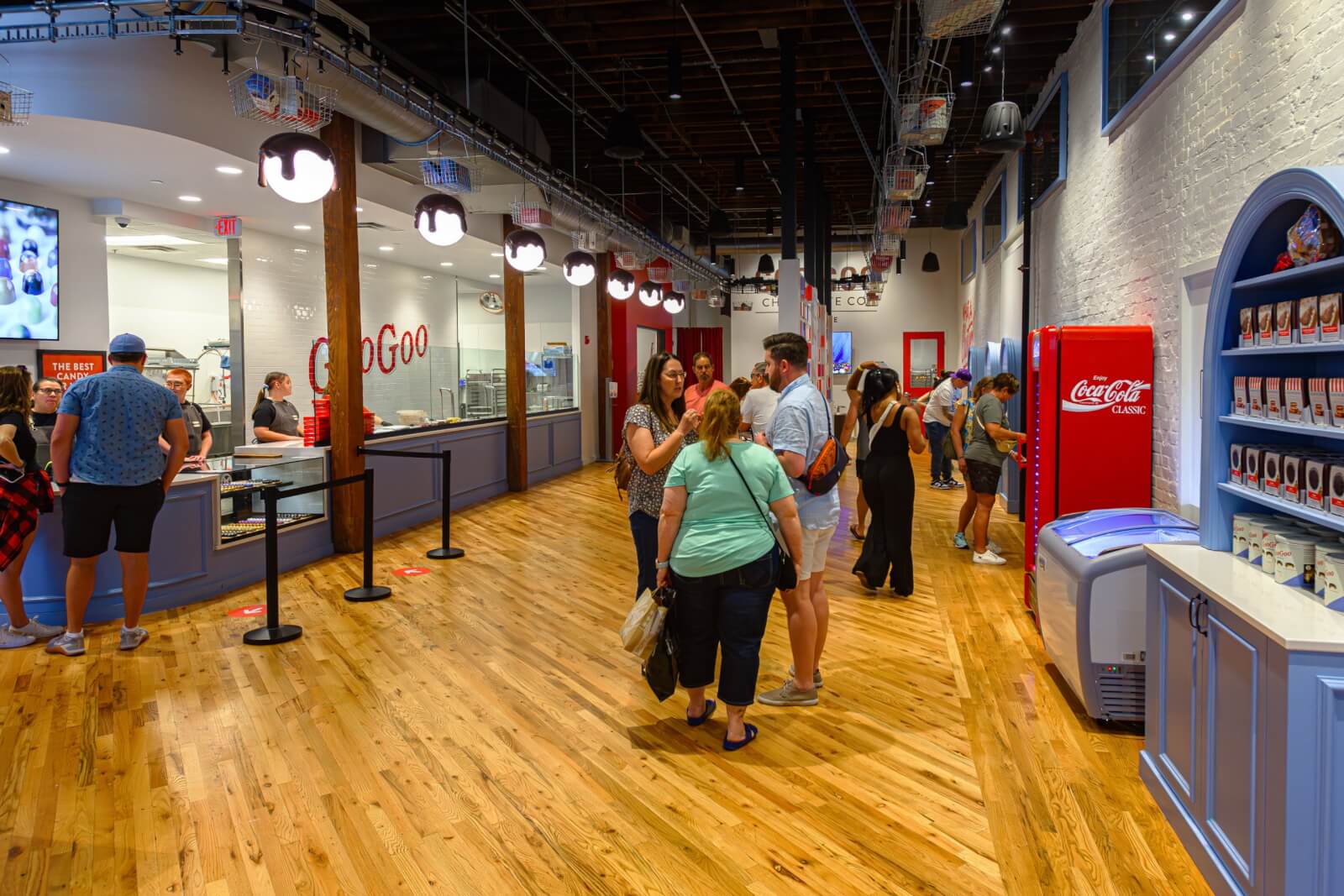People mingle and chat inside a brightly lit store with exposed brick walls, wooden floors, and a Coca-Cola vending machine—a quintessential Nashville event space that blends rustic charm with modern convenience.