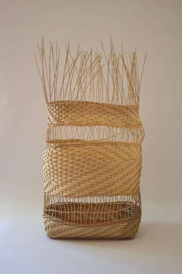 A woven basket with an irregular shape, featuring tightly woven sections and unfinished, protruding strands at the top—a unique find for those who seek luxe loves in artisanal design.