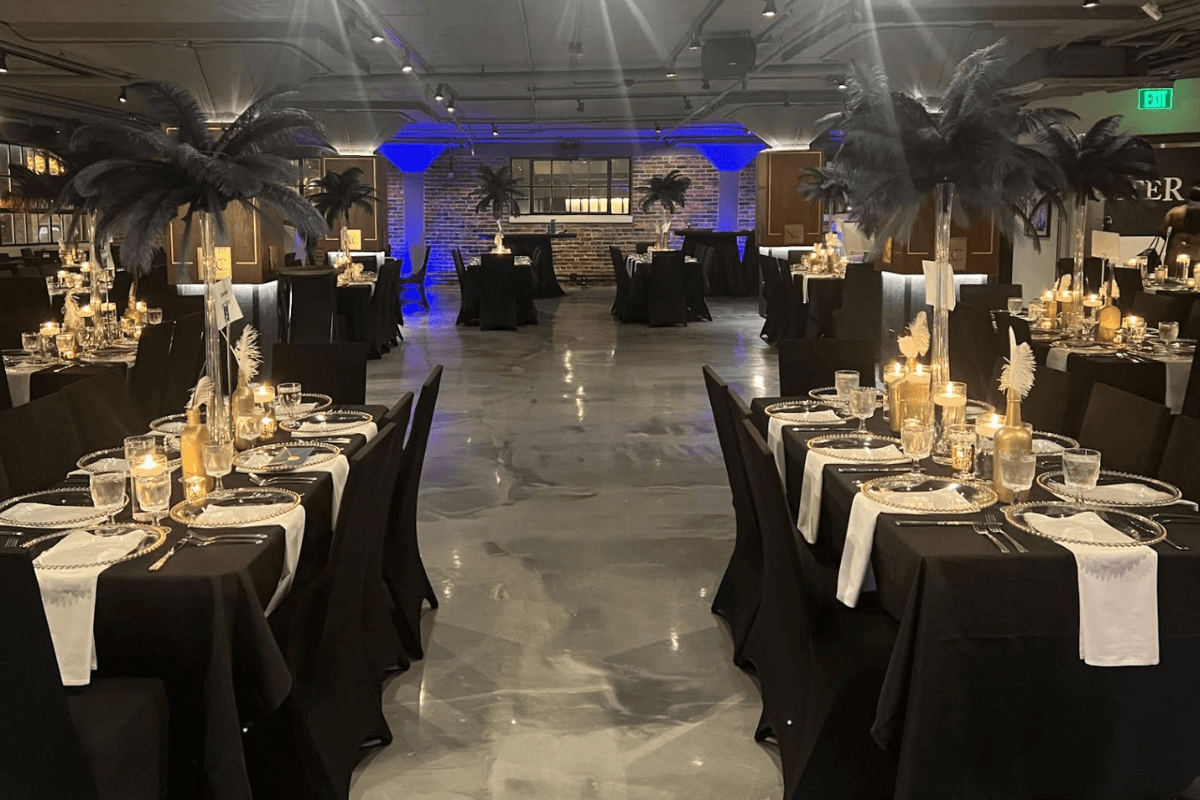 Elegant event setup in one of Nashville's finest event spaces, featuring tables draped in black tablecloths, adorned with candles and tall feather centerpieces. Dim lighting enhances the intimate atmosphere, making it an unforgettable occasion.