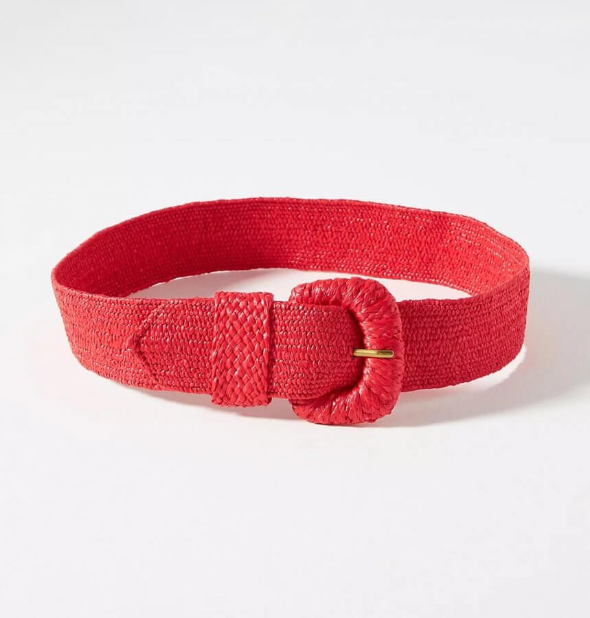 A red woven belt with a circular rattan buckle is laid flat on a white surface.