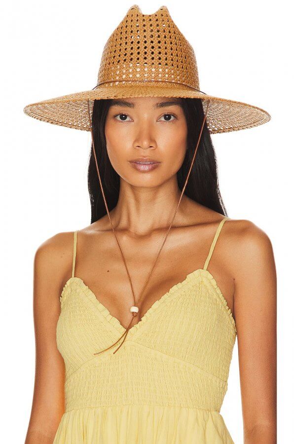 A person with long dark hair wears a wide-brimmed rattan hat and a yellow sundress.