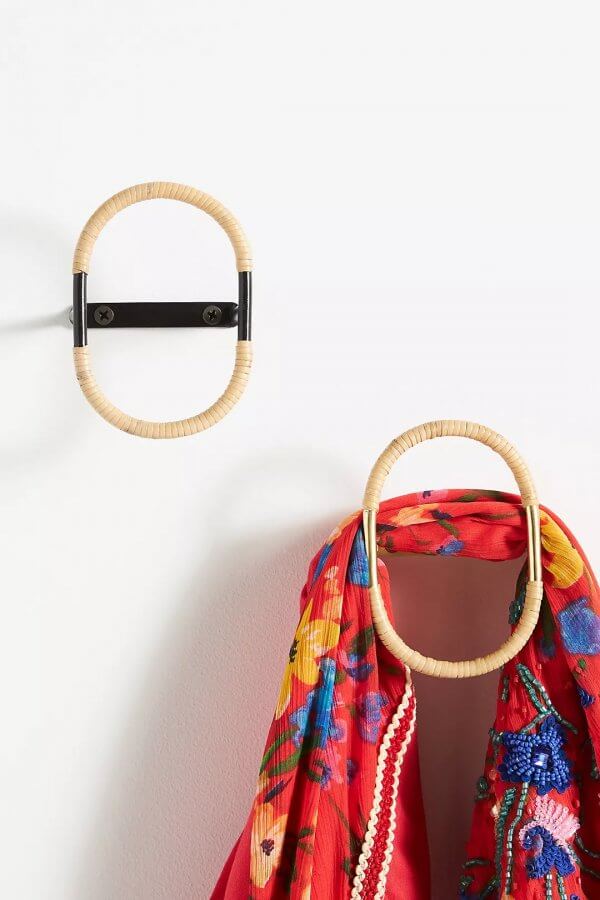 A black metal hook with a tan rattan loop is mounted on a white wall. An identical hook below it holds a bright red floral scarf.