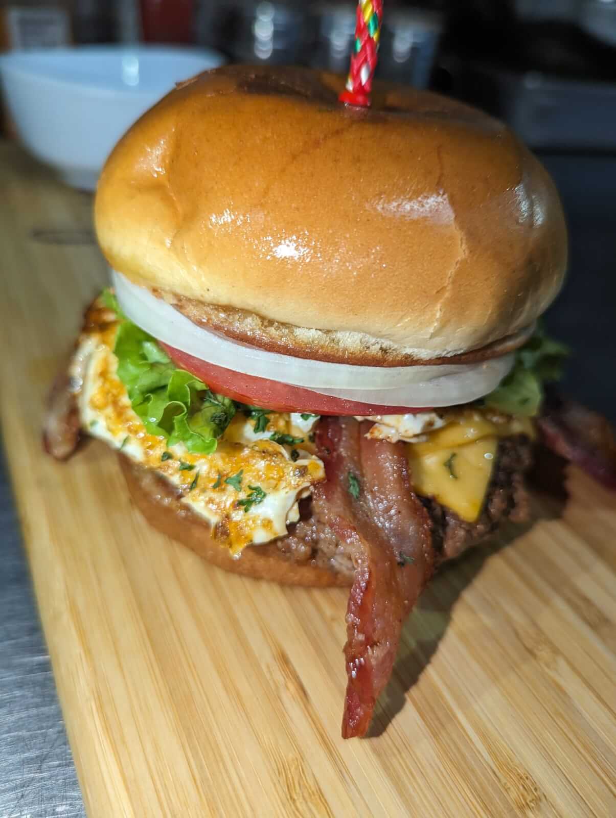 A close-up of a burger with bacon, lettuce, tomato, onion, and cheese on a wooden board at one of the new Louisville restaurants.