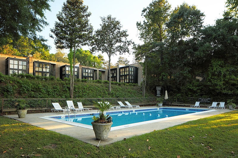 Outdoor swimming pool surrounded by lounge chairs and potted plants, with modern black and white buildings and trees in the background, capturing the serene charm of South Carolina.