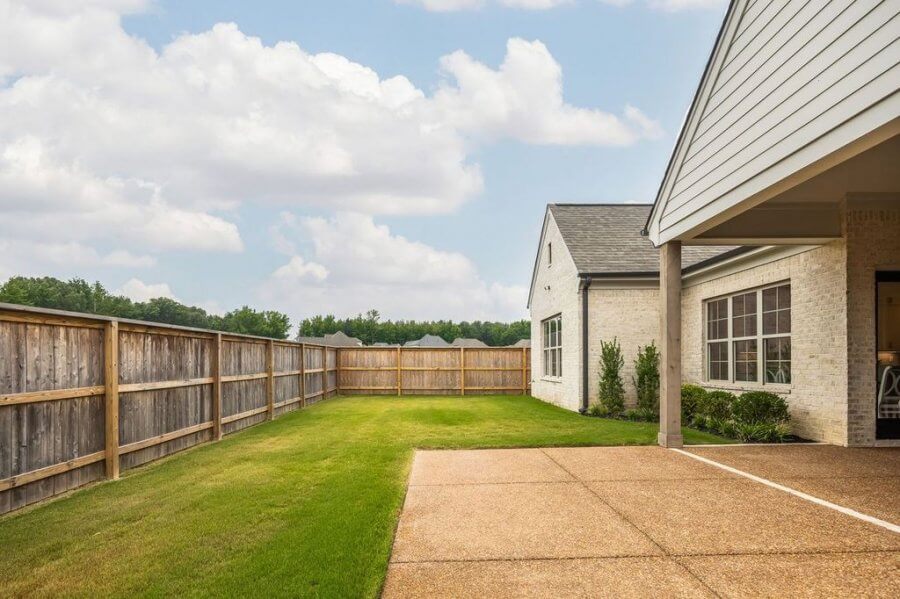 A fenced backyard with a green lawn, a paved patio area, and the exterior of a light-colored house on Magnolia Ridge Drive in Rossville, Tennessee, all under a partly cloudy sky.