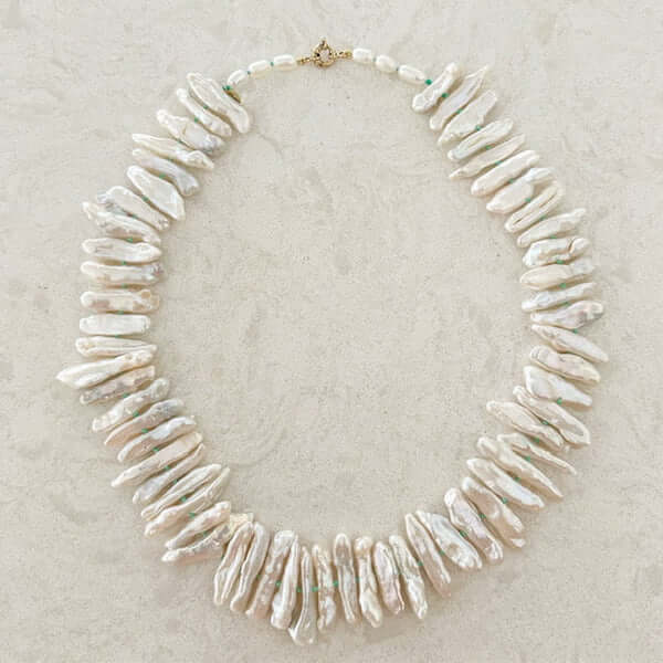 A necklace made of irregularly shaped white baroque pearls with a gold clasp, displayed on a light textured surface—a piece for those with luxe loves.