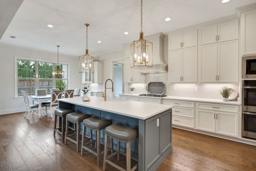 Modern kitchen on Magnolia Ridge Drive, Rossville Tennessee, features white cabinets, stainless steel appliances, a large island with gray stools, pendant lighting, and an adjoining dining area with windows.
