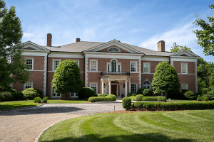 A large, two-story brick house located at 11 Overbrook Road in Louisville, KY features symmetrical architecture, columns at the entrance, and well-maintained landscaping with shrubbery and trees, all under a clear blue sky.