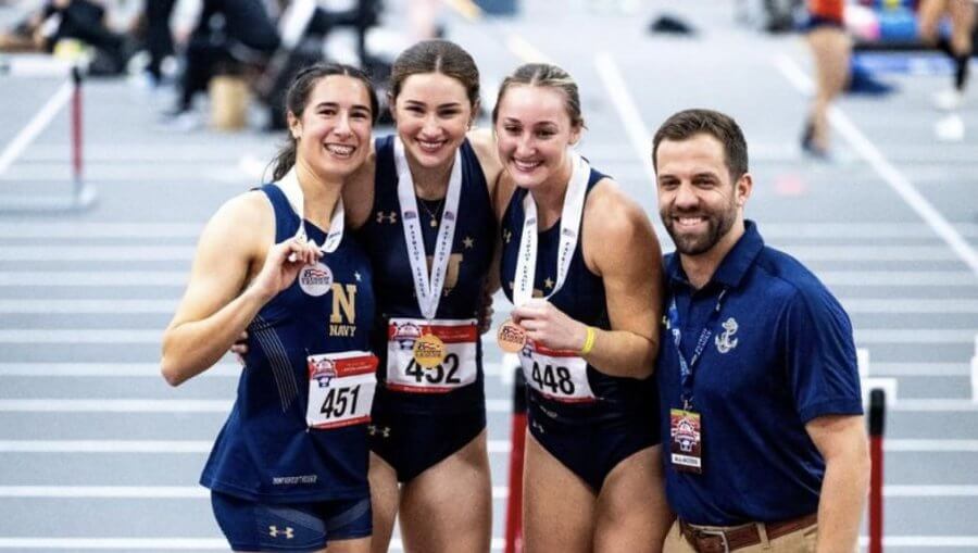 Three members of the Navy Women's Track Team smile and pose on an track field at the Naval Academy, after a competition.