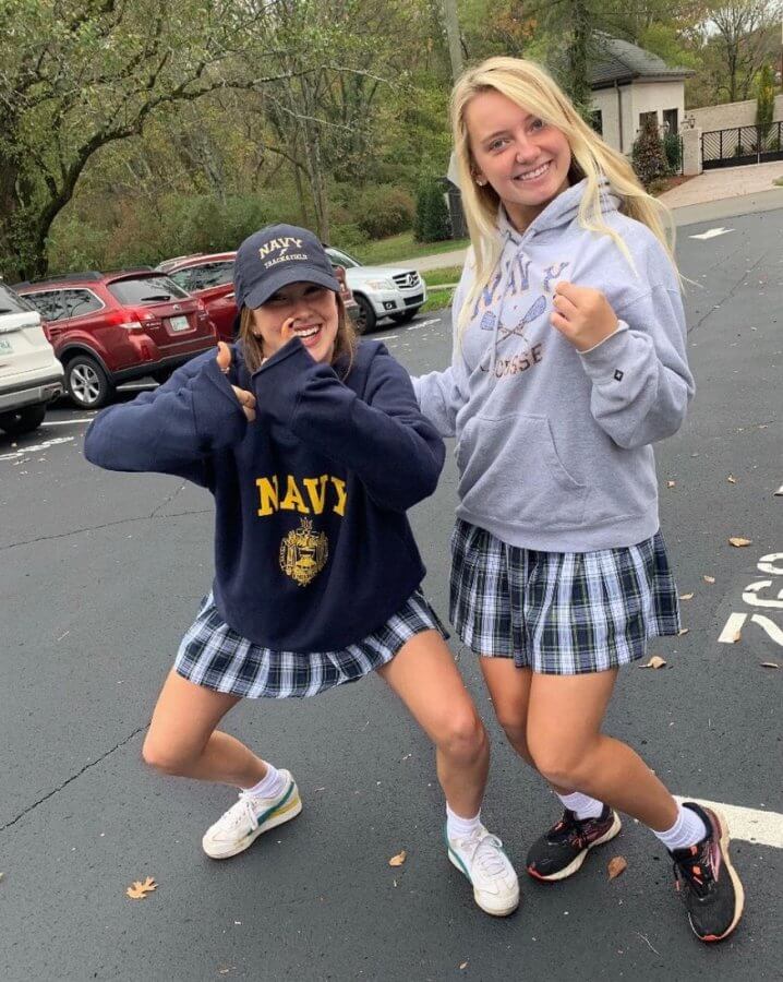 Annie Taylor and Leelee Denton with their naval academy sweatshirts and Harpeth Hall plaid skirts pose playfully in a parking lot. 