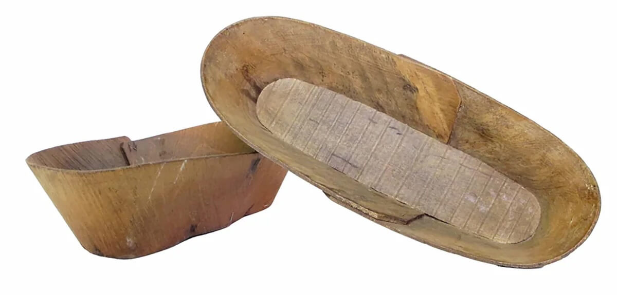 Two wooden trenchers, one leaning on the other. The wood appears worn and weathered, indicating frequent use. Simple and functional in design with a rustic appearance.