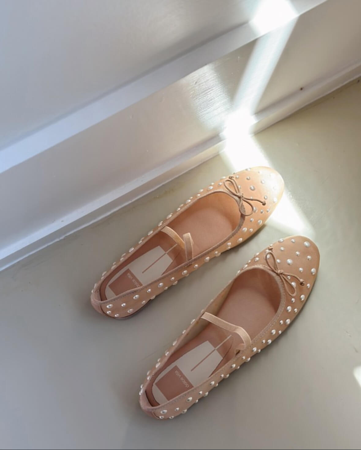 A pair of nude-colored, polka-dotted flats with small bows on the toes, placed on a light-colored floor in a Nashville boutique, with sunlight streaming in.