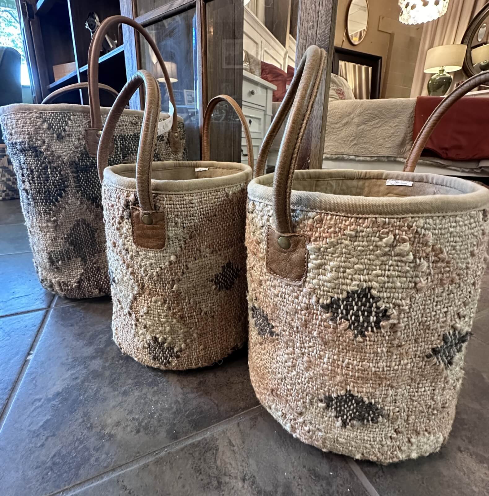 Three woven baskets with handles in varying sizes sit on a tiled floor, showcasing a textured, geometric pattern. These elegant pieces are the perfect FINDS for your Nashville home this September.