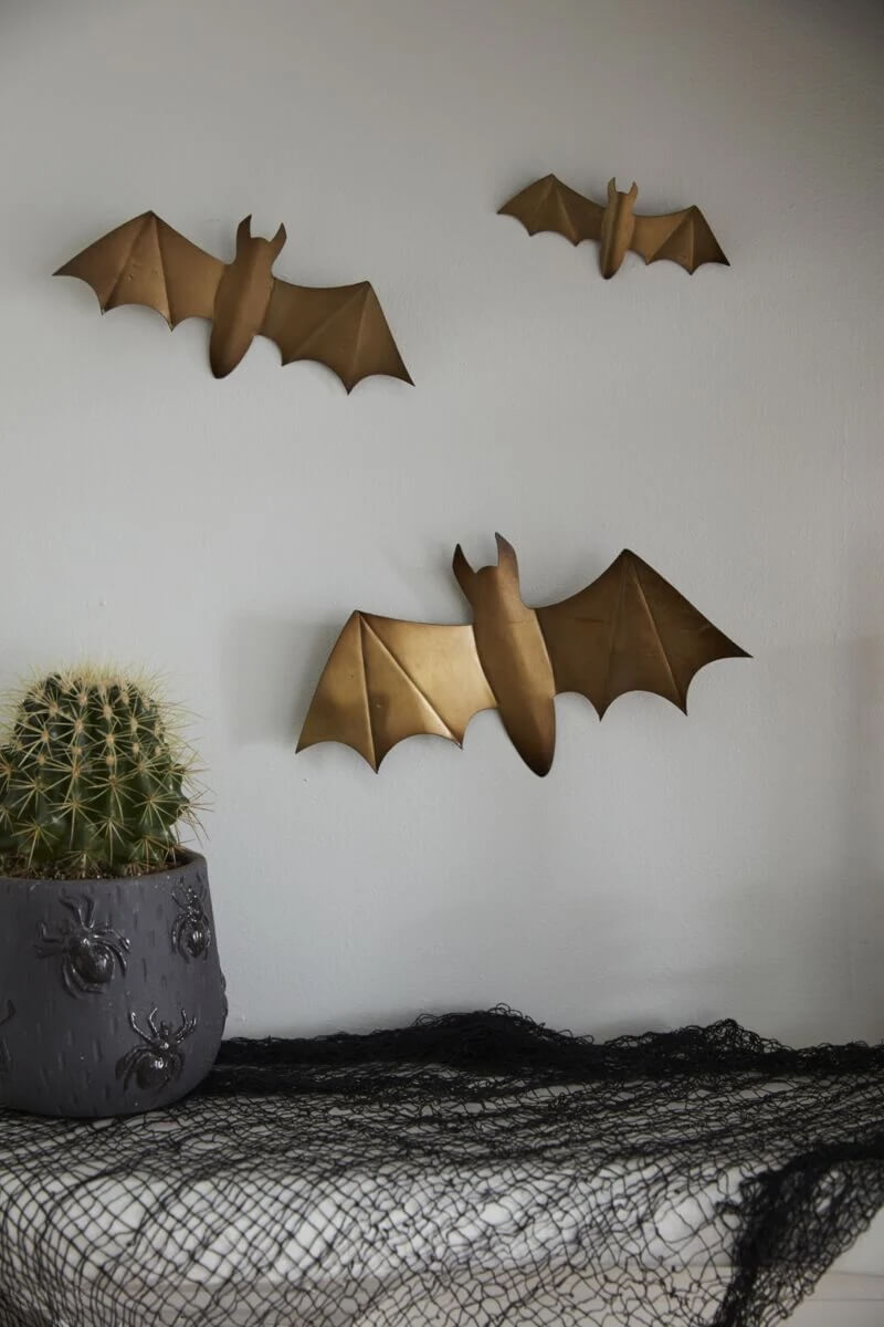 Metal bat decorations on a wall above a cactus in a pot with face designs, all placed on a table covered with black netting.