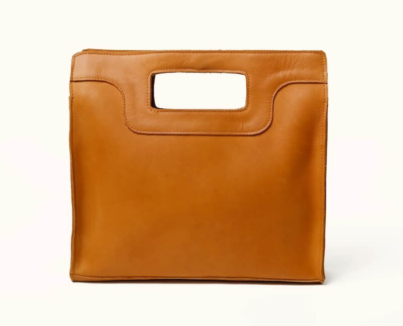 A brown leather handbag with a rectangular cut-out handle, perfect for your September outings in Nashville. The bag boasts a smooth texture and an elegant rectangular shape.